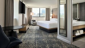 Hotelkamer met een bed, bureau, stoel, televisie, badkamer met spiegel en uitzicht op de stad.