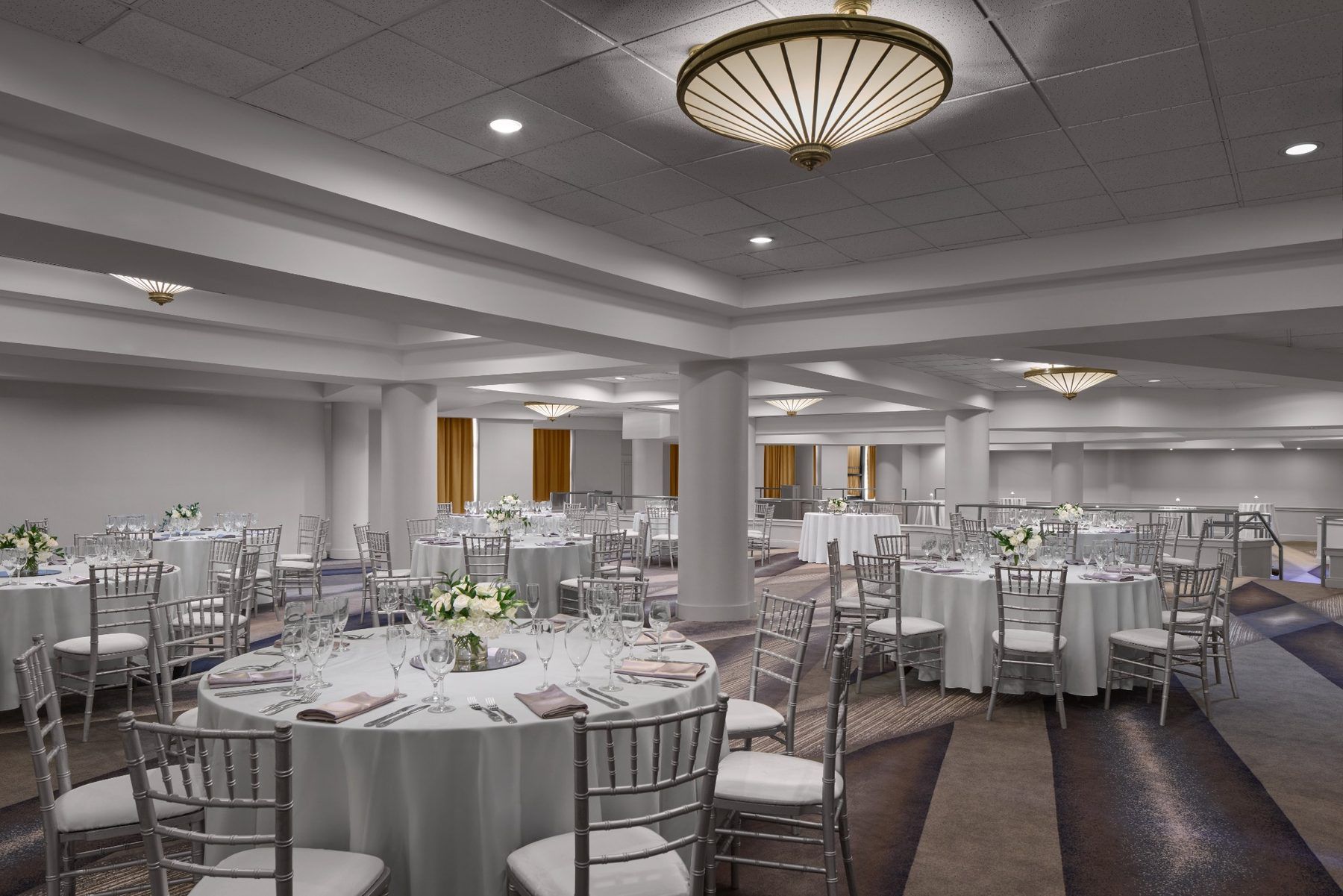 A large, well-lit banquet hall with multiple round tables, each set with chairs and table settings.