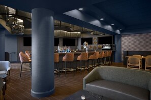 A modern bar area with a high ceiling, a central column, and bar stools. - Sheraton Baltimore North Hotel (Towson)