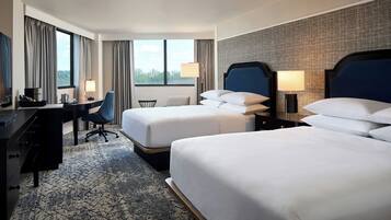A hotel room with two beds, a desk, a chair, and a view of the outdoors.