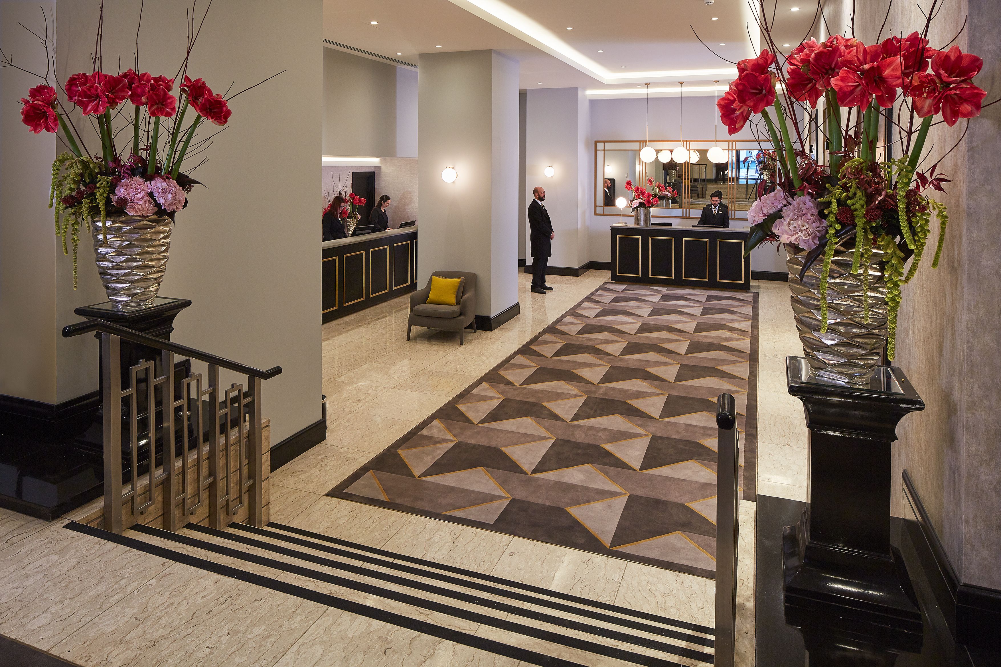 A hotel lobby with a reception desk, a check-in counter, and a large decorative vase with flowers.