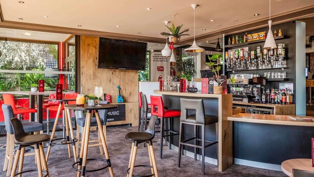 A modern bar with red and black bar stools, a flat-screen TV, and a variety of bottles on shelves. - ibis Colmar Est (Horbourg-Wihr)