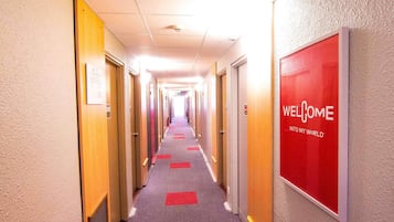 A hotel hallway with doors on both sides, a red 'WELCOME' sign on the right, and a carpeted floor.