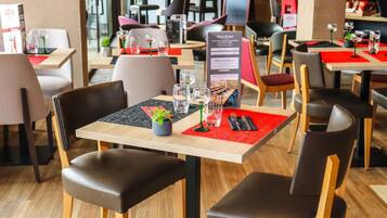 Un interior de restaurante con mesas de madera, sillas de cuero negro y manteles individuales rojos.