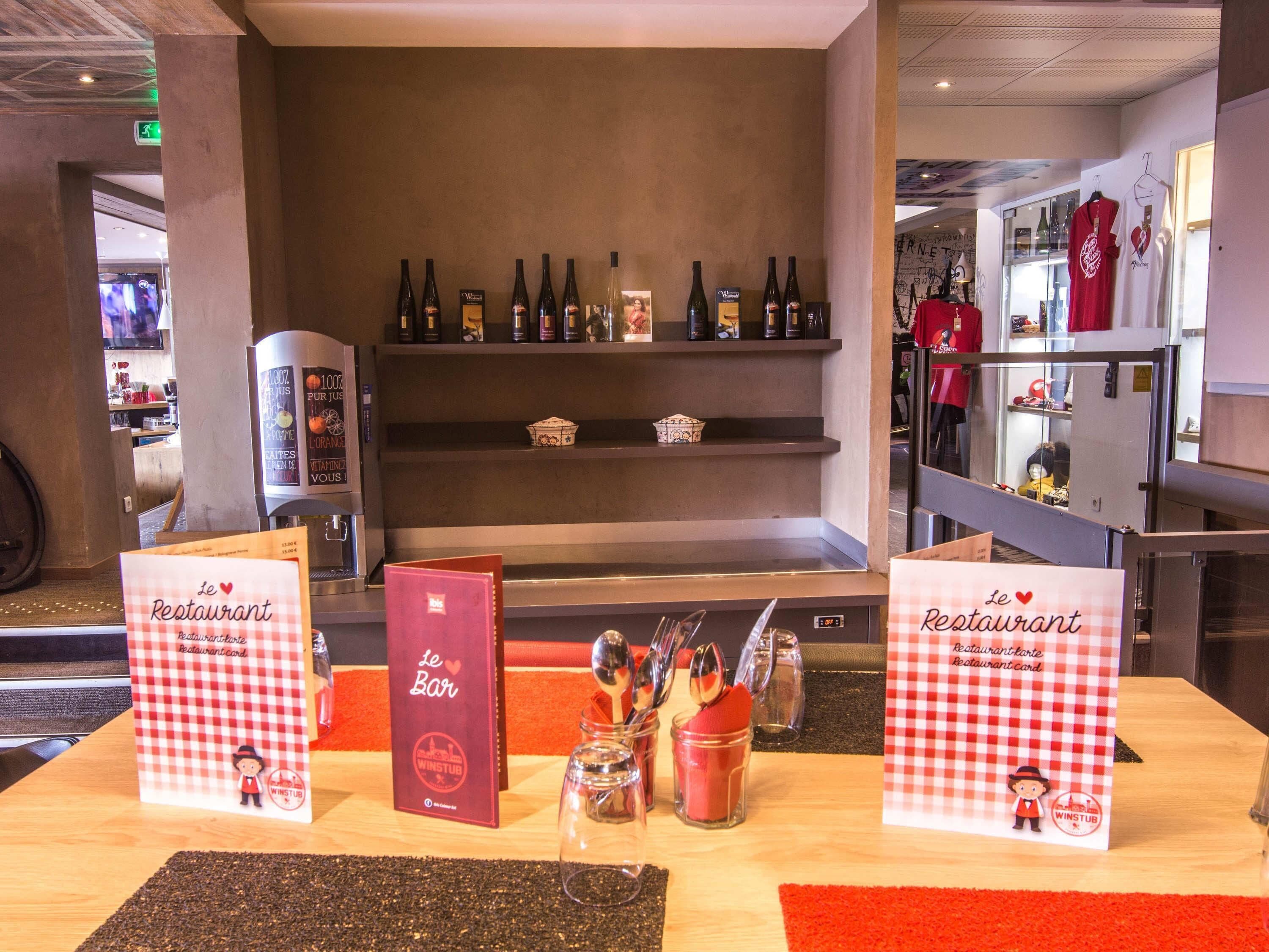 Interior de un restaurante con zona de bar, botellas de vino en estanterías y un atril con la carta.