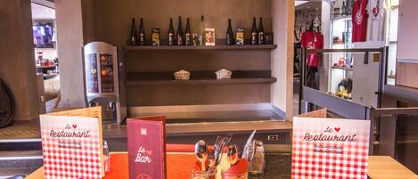Interior de un restaurante con zona de bar, botellas de vino en estanterías y un atril con la carta.