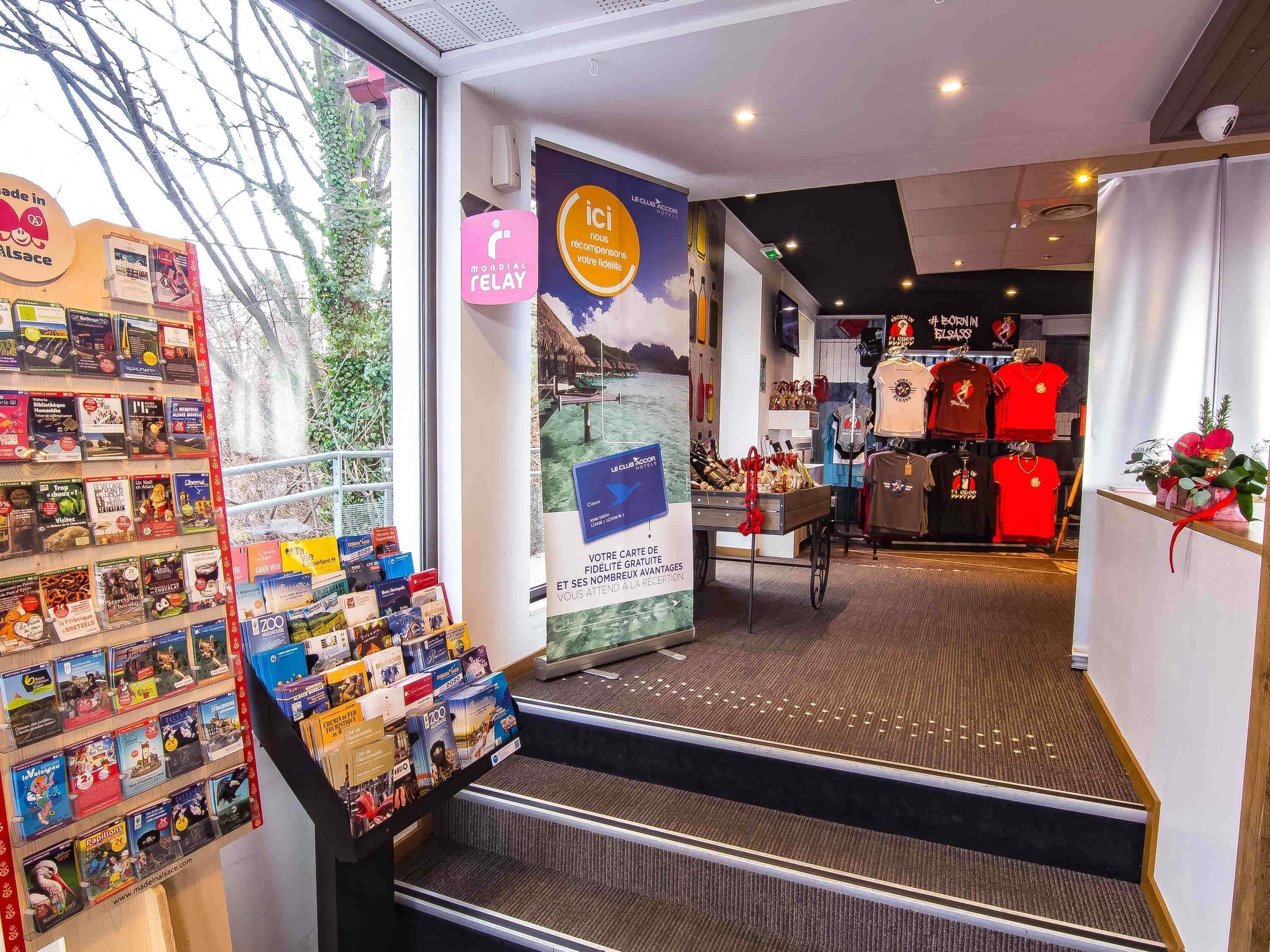 A bookstore with a variety of books and magazines on display, a poster advertising a club, and a staircase leading to another section.