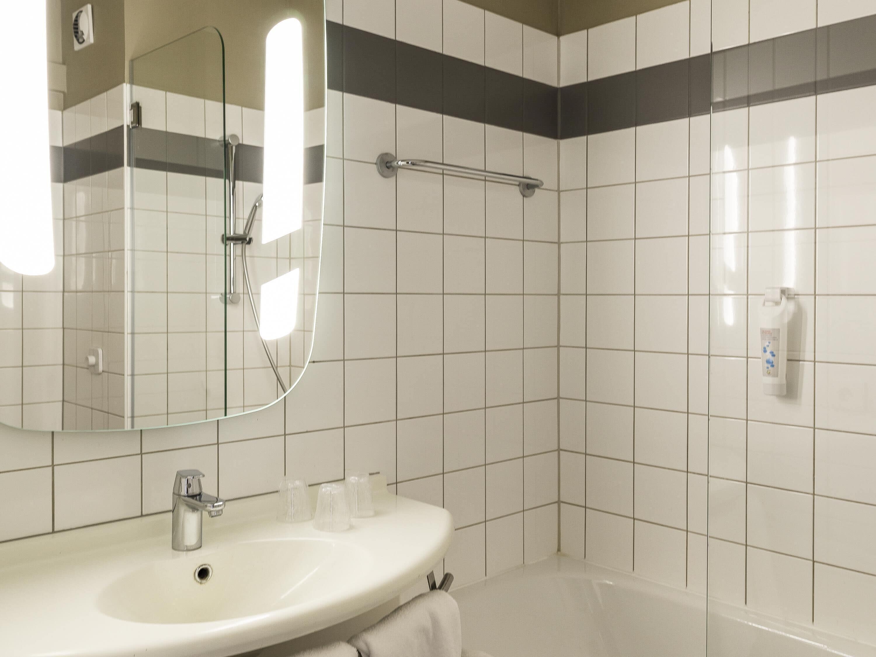 A bathroom with a sink, mirror, shower, and hand dryer.