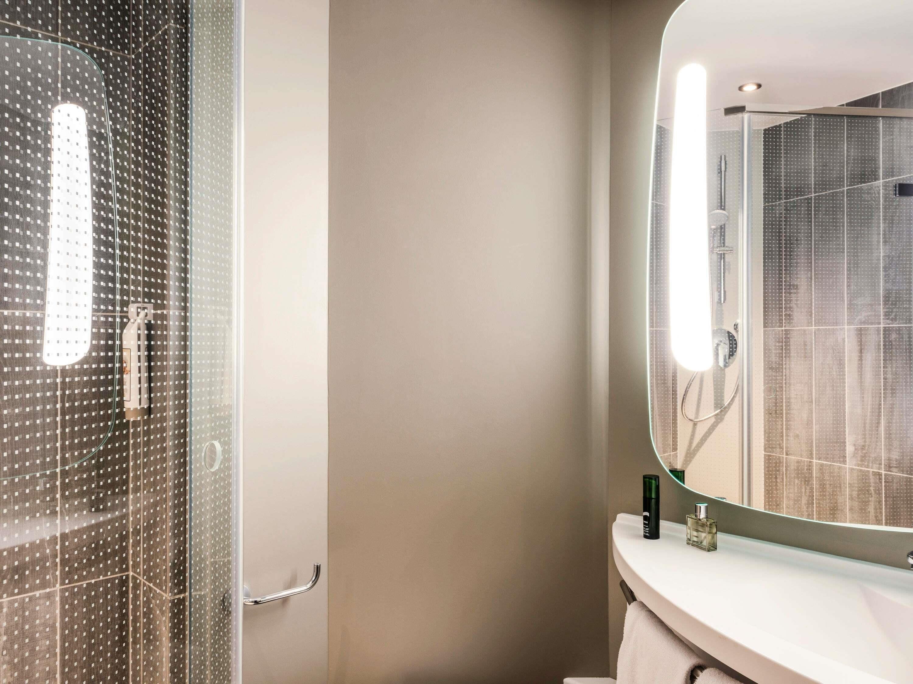 A bathroom with a glass shower enclosure, a white sink, and a mirror reflecting the shower area.