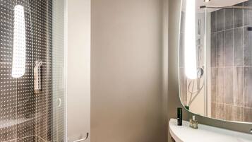A bathroom with a glass shower enclosure, a white sink, and a mirror reflecting the shower area.