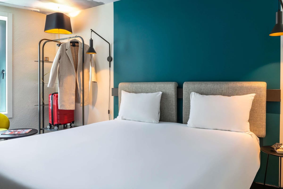 Une chambre d’hôtel avec un grand lit, deux tables de chevet, une armoire et une valise.