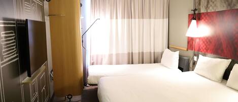 A hotel room with two beds, a red carpet, a wooden door, a large window with curtains, and a wall with a red and grey pattern.
