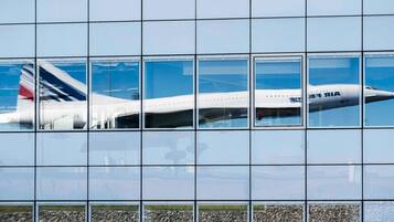 A modern building with a glass facade reflecting an airplane.