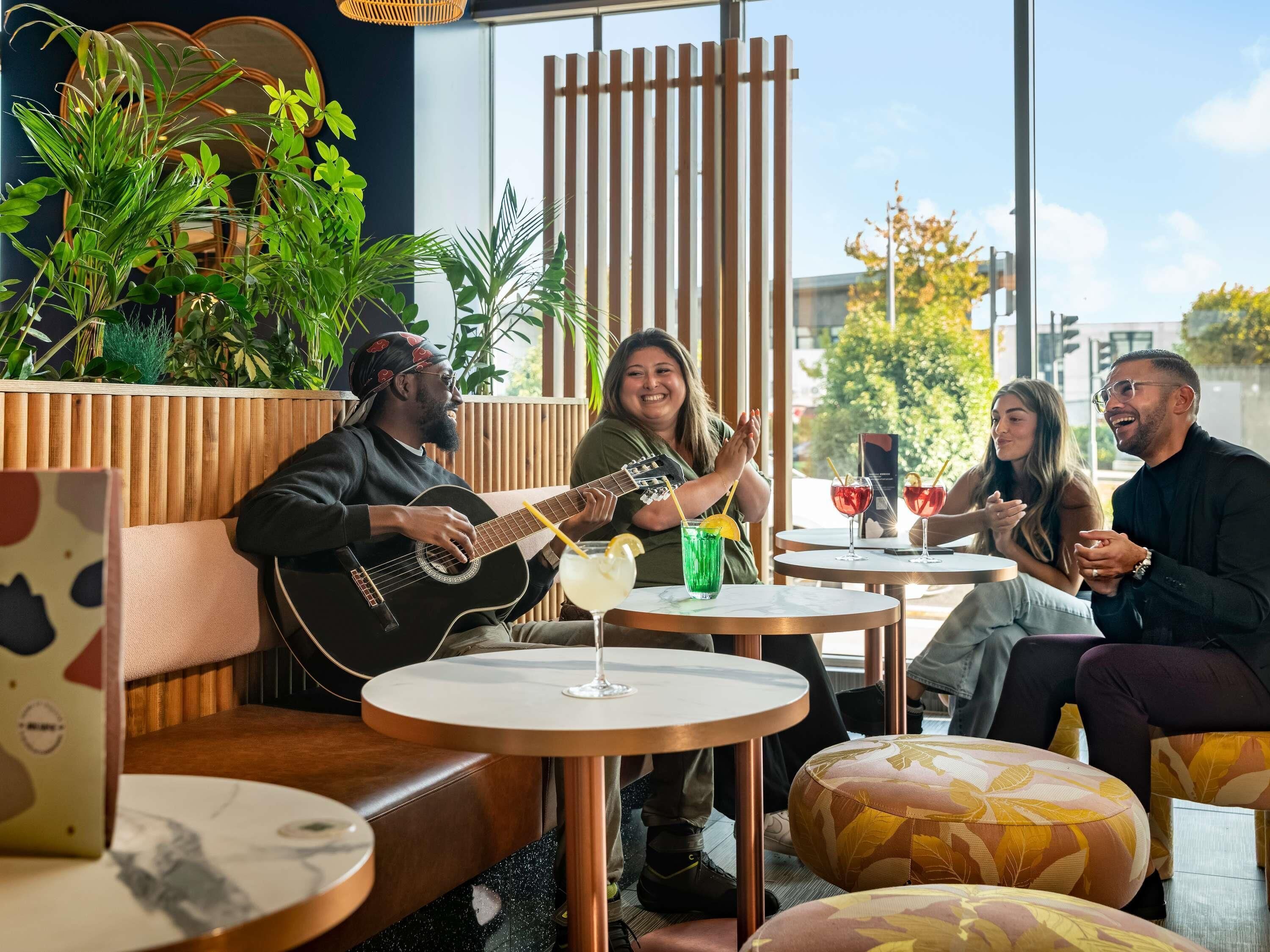 A group of people seated in a modern indoor setting with wooden accents and plants.
