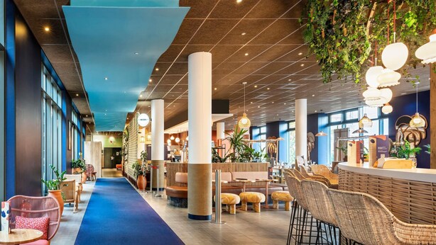 Un hall d’hôtel moderne avec un tapis bleu, des meubles en osier et un coin bar.