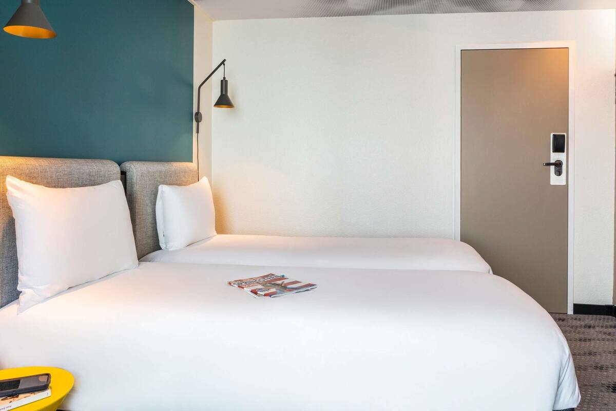 Een hotelkamer met een bed, nachtkastje, lamp en een deur.