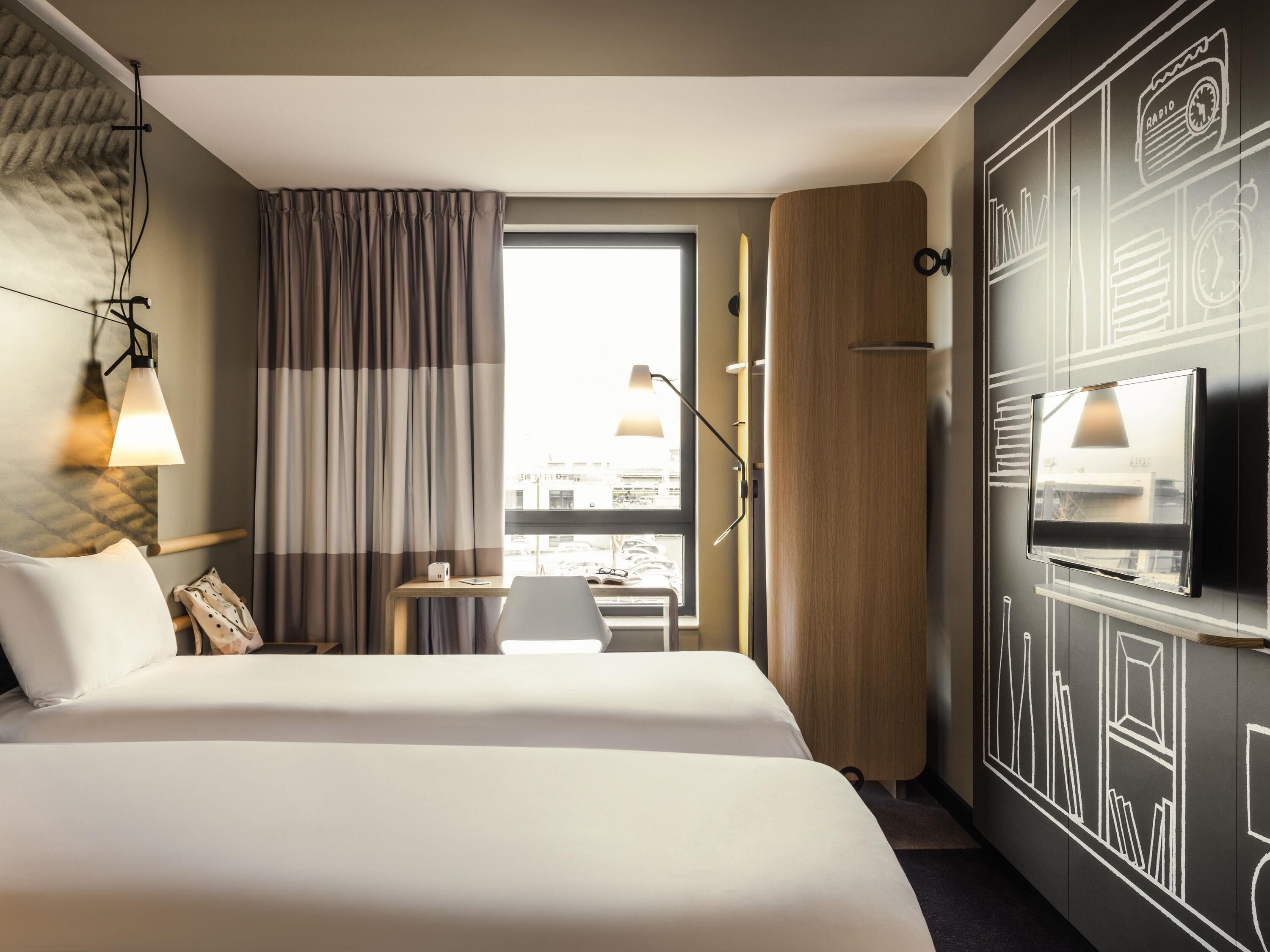 Een hotelkamer met een groot bed, een bureau met stoel, een televisie en een raam met gordijnen.