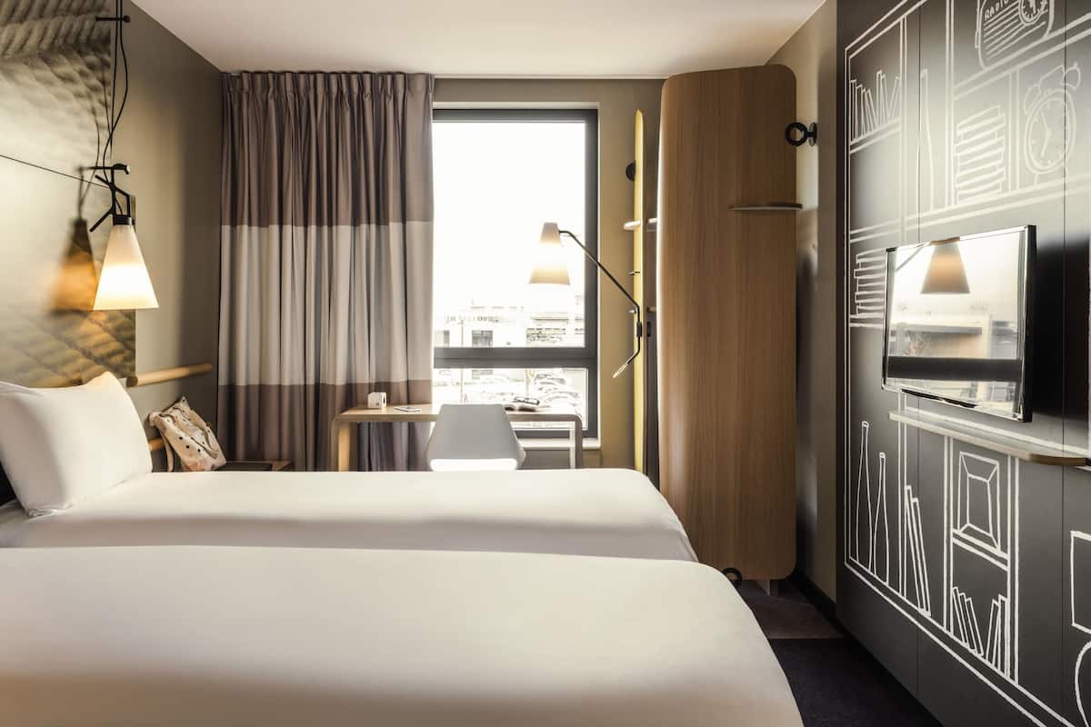 Une chambre d’hôtel avec un grand lit, un bureau avec une chaise, une télévision et une fenêtre avec des rideaux.