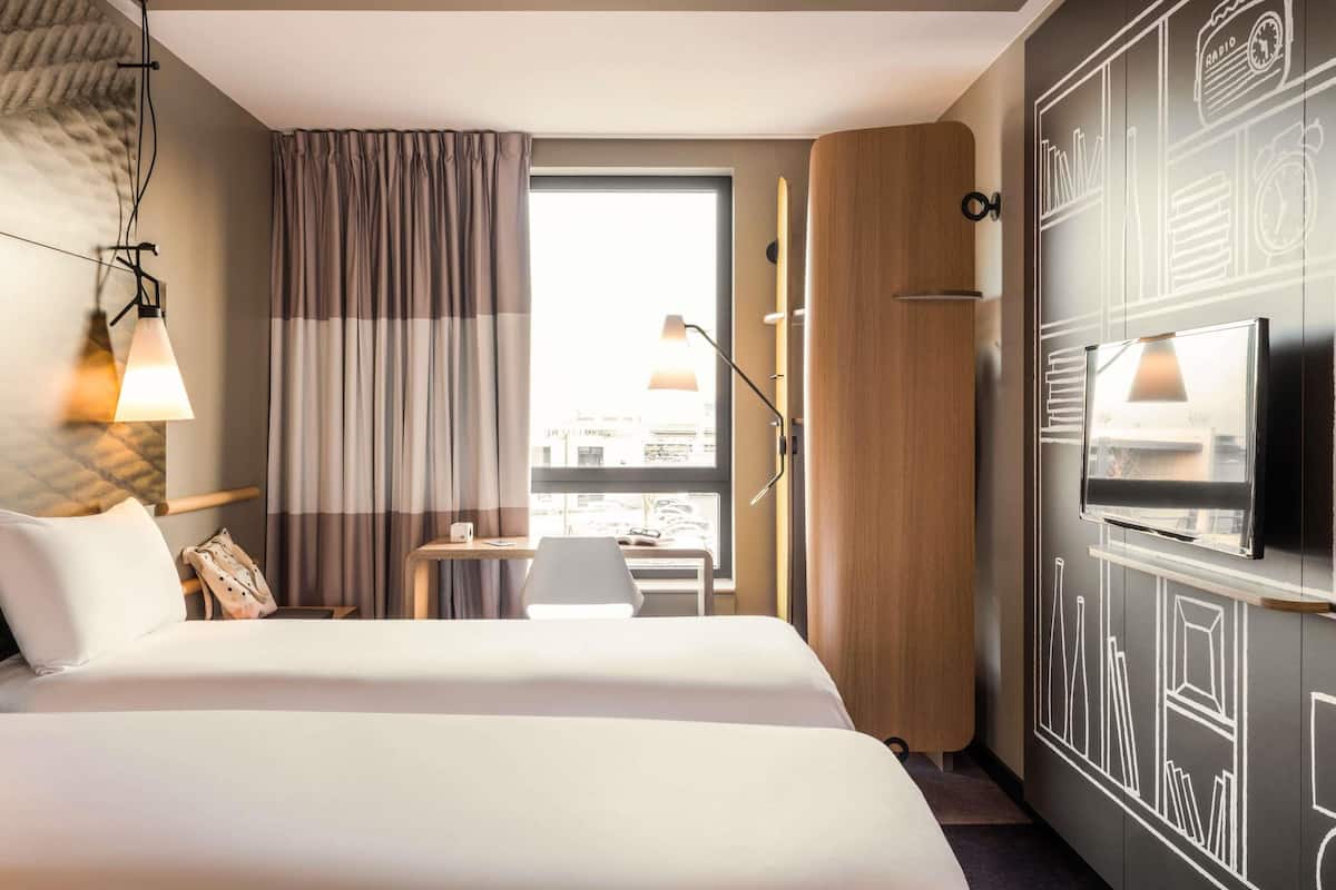 Une chambre d’hôtel avec un grand lit, un bureau, une télévision et une fenêtre avec des rideaux.