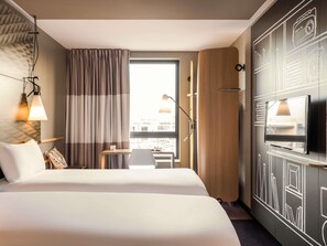 A hotel room with a large bed, a desk, a TV, and a window with curtains.