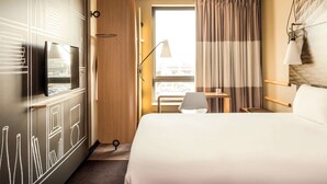 Une chambre d’hôtel avec un lit, un bureau, une chaise, une télévision et une fenêtre avec des rideaux.