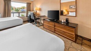 Une chambre d’hôtel avec deux lits, un bureau avec une télévision, une commode et une fenêtre avec des rideaux.