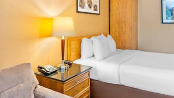 Quarto de hotel com cama, mesa de cabeceira com abajur, telefone e guarda-roupa de madeira.