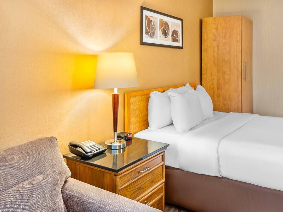 Quarto de hotel com cama, mesa de cabeceira com abajur, telefone e guarda-roupa de madeira.