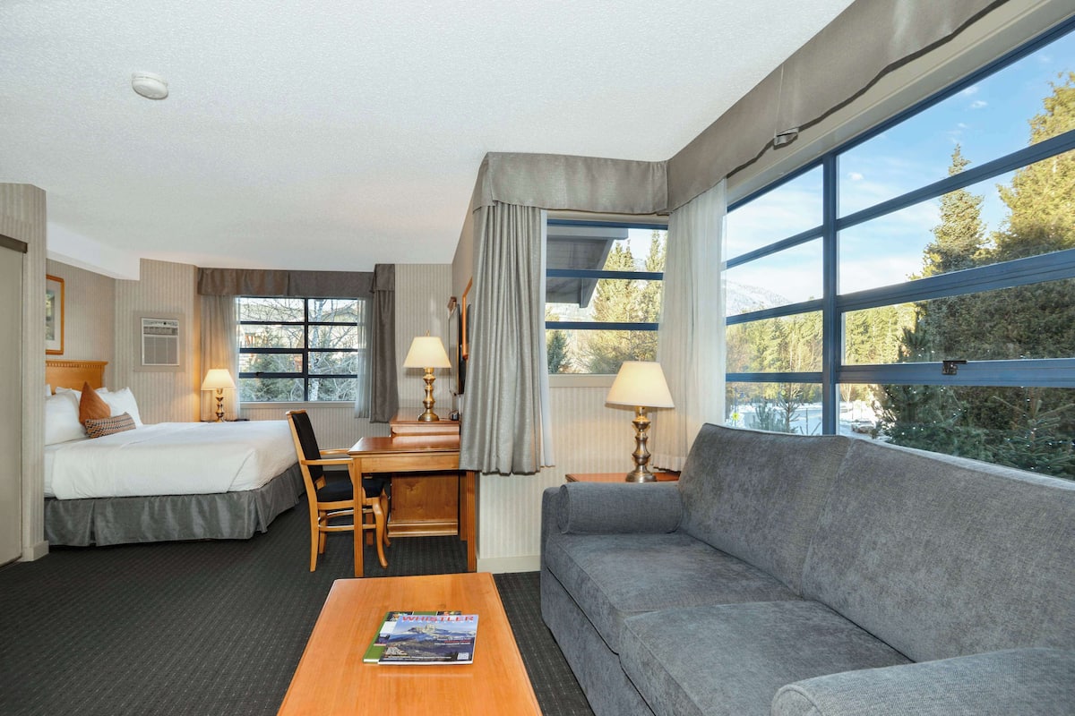 A hotel room with a bed, a desk, a chair, a sofa, and a coffee table.
