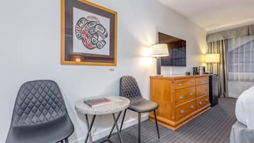 Une chambre d’hôtel avec un lit, un bureau et une chaise, une petite table avec un livre, une lampe, une commode et une œuvre d’art encadrée accrochée au mur.