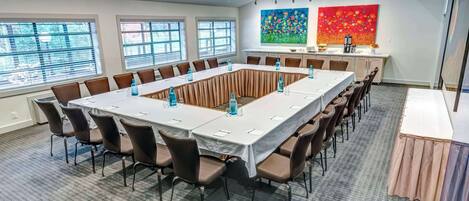 Un salón de conferencias con una larga mesa, sillas y una pequeña cocina.