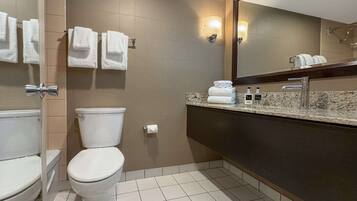A bathroom with a toilet, a sink with a mirror, and towels on the wall.