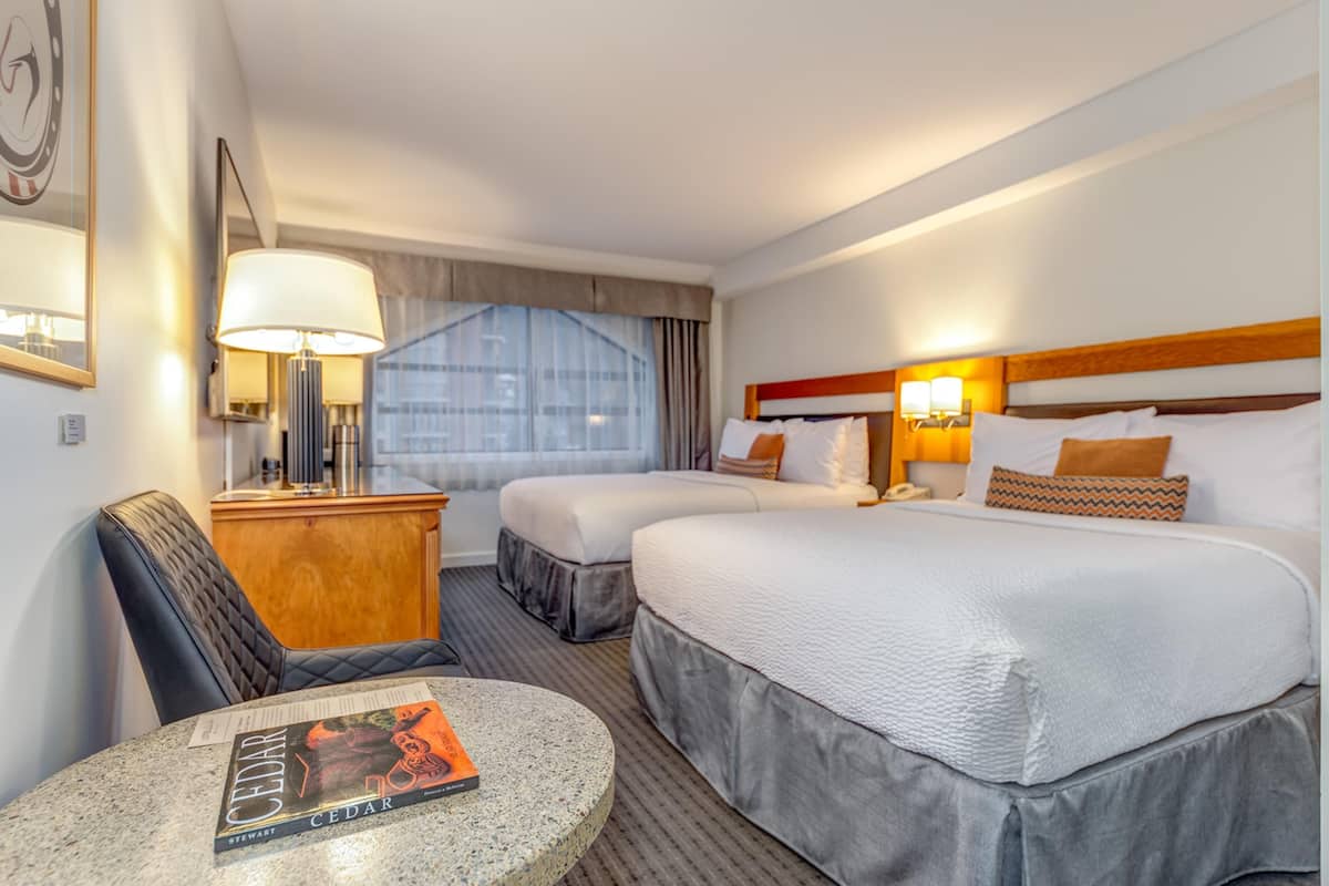 A hotel room with two beds, a desk, a chair, a lamp, and a window with curtains.