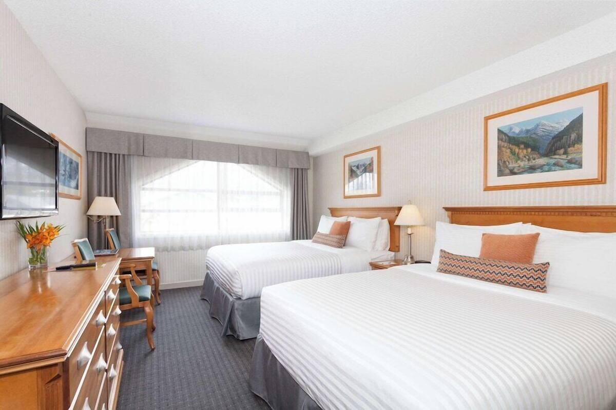 A hotel room with two beds, a desk, and a TV.