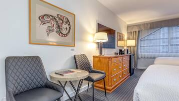 A hotel room with a bed, two armchairs, a small round table, a wooden dresser, and a large window with curtains.