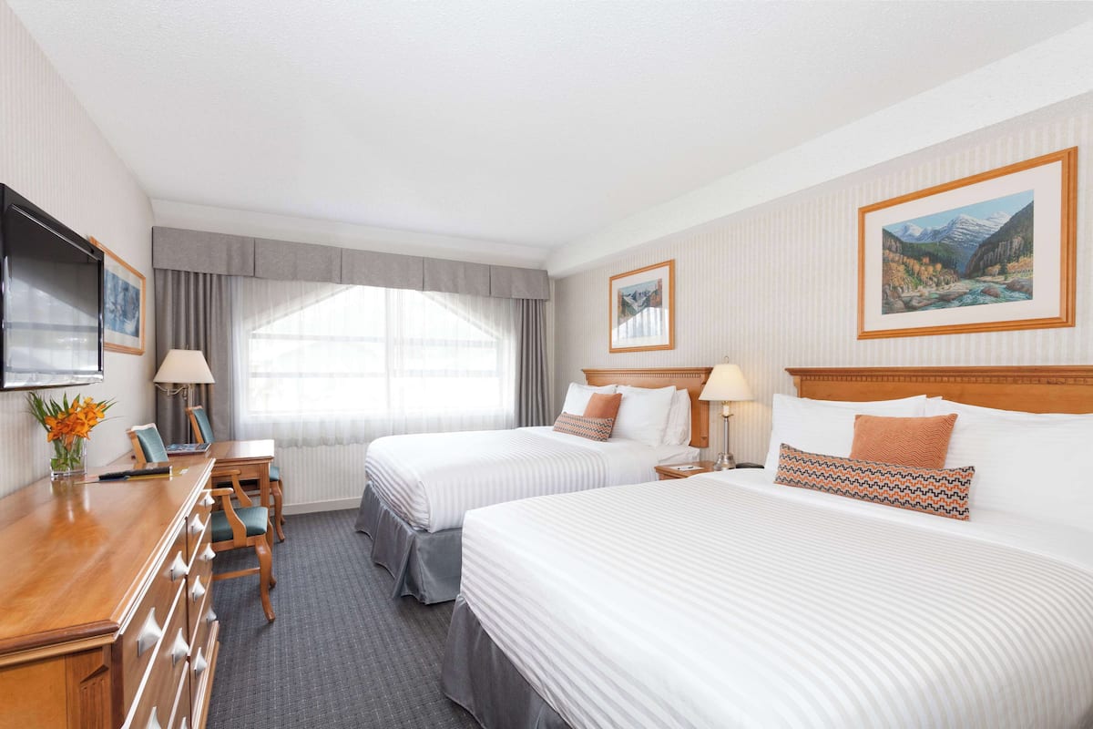 A hotel room with two beds, a desk, a chair, a TV, and a window with curtains.