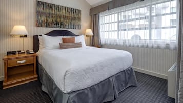 A hotel room with a large bed, two bedside tables with lamps, a modern abstract painting on the wall, and a large window with sheer curtains.