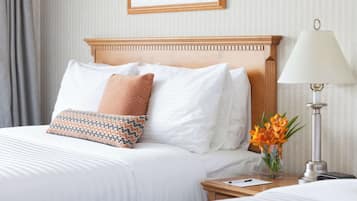 A neatly made bed with white linens and patterned pillows, a bedside table with a lamp and a vase of flowers, and a framed picture on the wall.