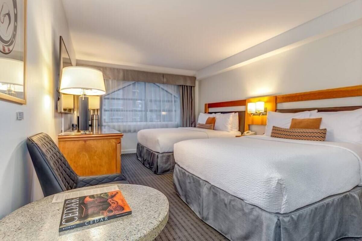 A hotel room with two beds, a desk, a chair, a round table, and a window with curtains.