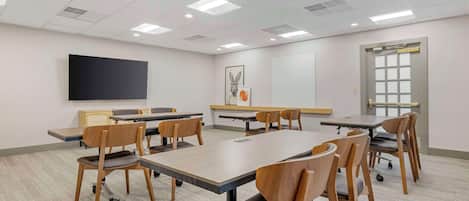 A conference room with a large flat-screen TV, a whiteboard, and a window with blinds.