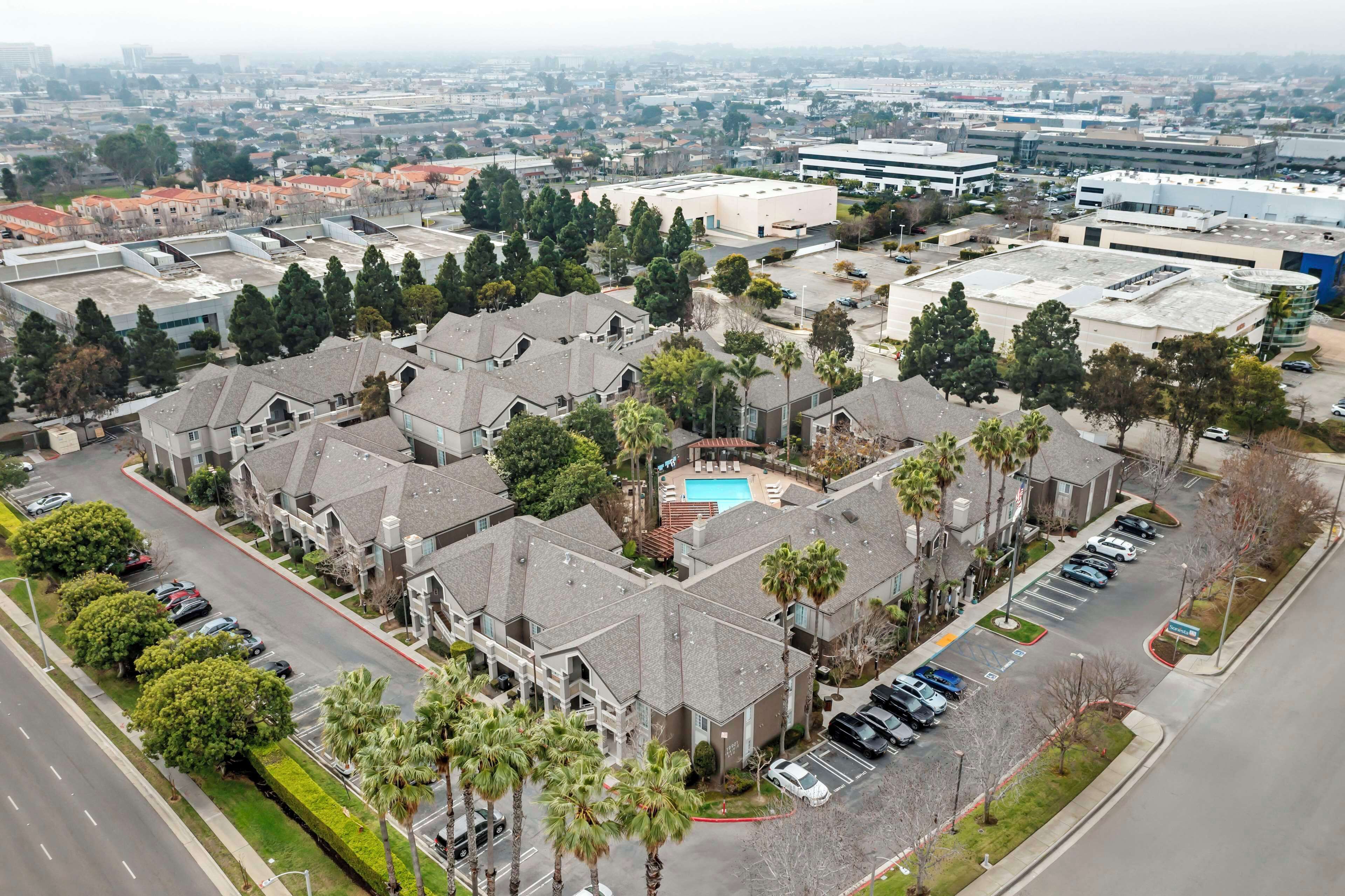 An aerial view of a residential area with multiple buildings, a swimming pool, and a parking lot.