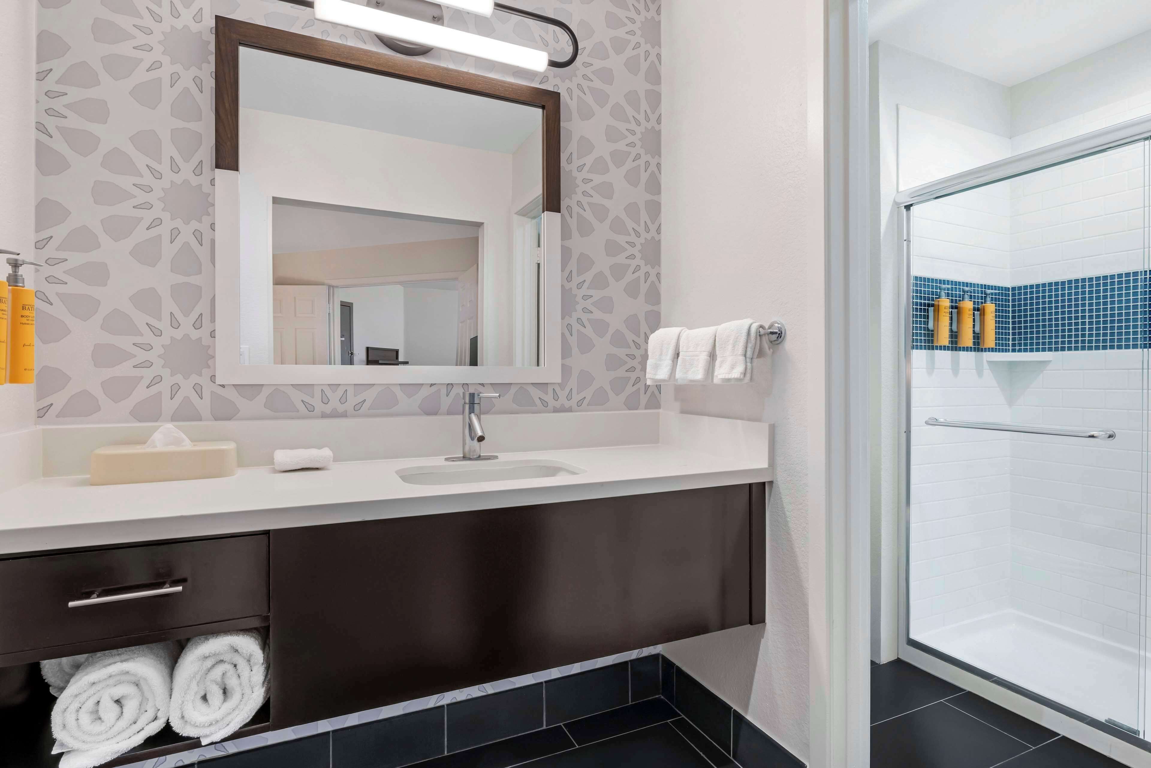 A modern bathroom with a large mirror, dark cabinetry, and a shower area with blue tiles.