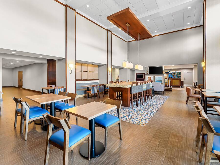 A spacious dining area with multiple tables and chairs, a central bar, and a television screen.