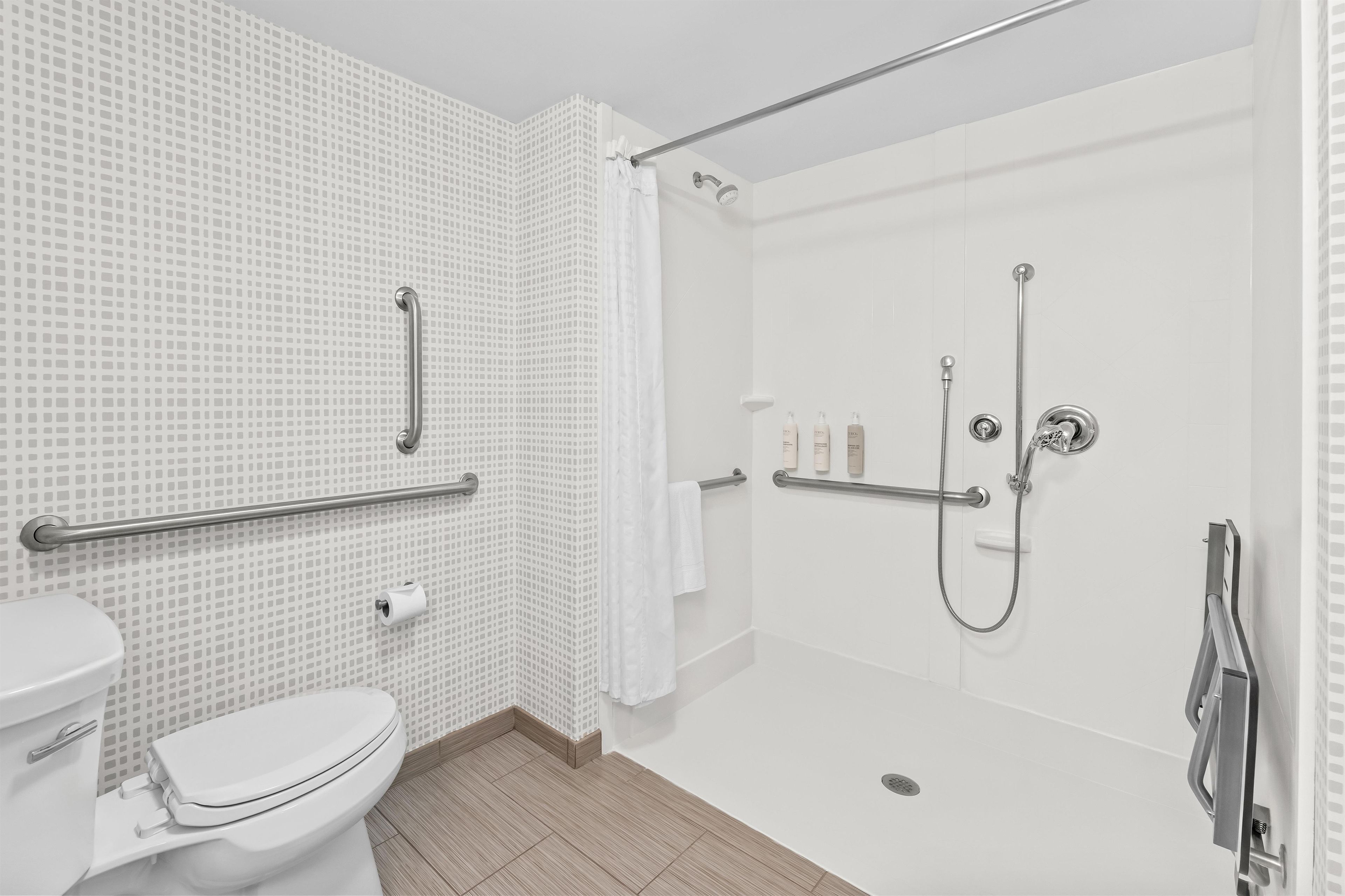 A modern bathroom with a toilet, a shower with a glass door, and a grab bar for safety.
