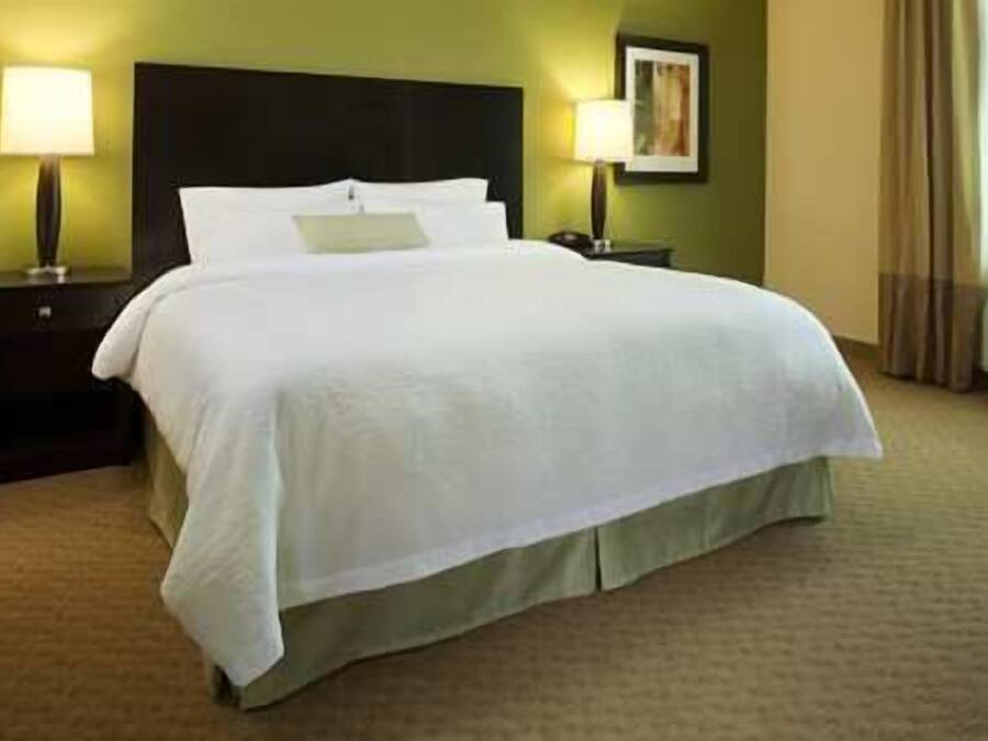 A neatly made bed with white linens in a hotel room with green walls, a dark headboard, and two bedside lamps.