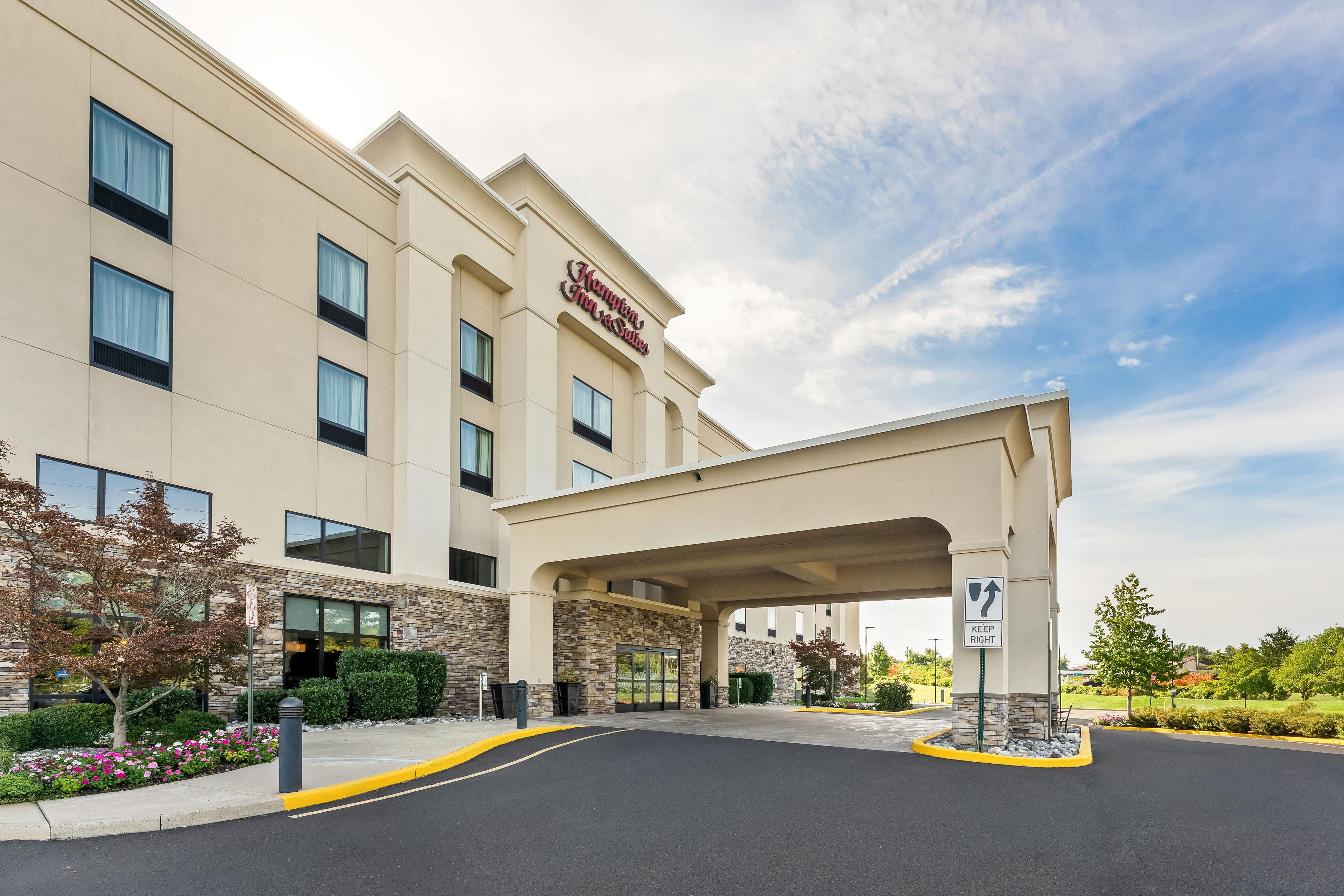 A Hampton Inn & Suites hotel with a modern facade, a covered entrance, and a clear sky.