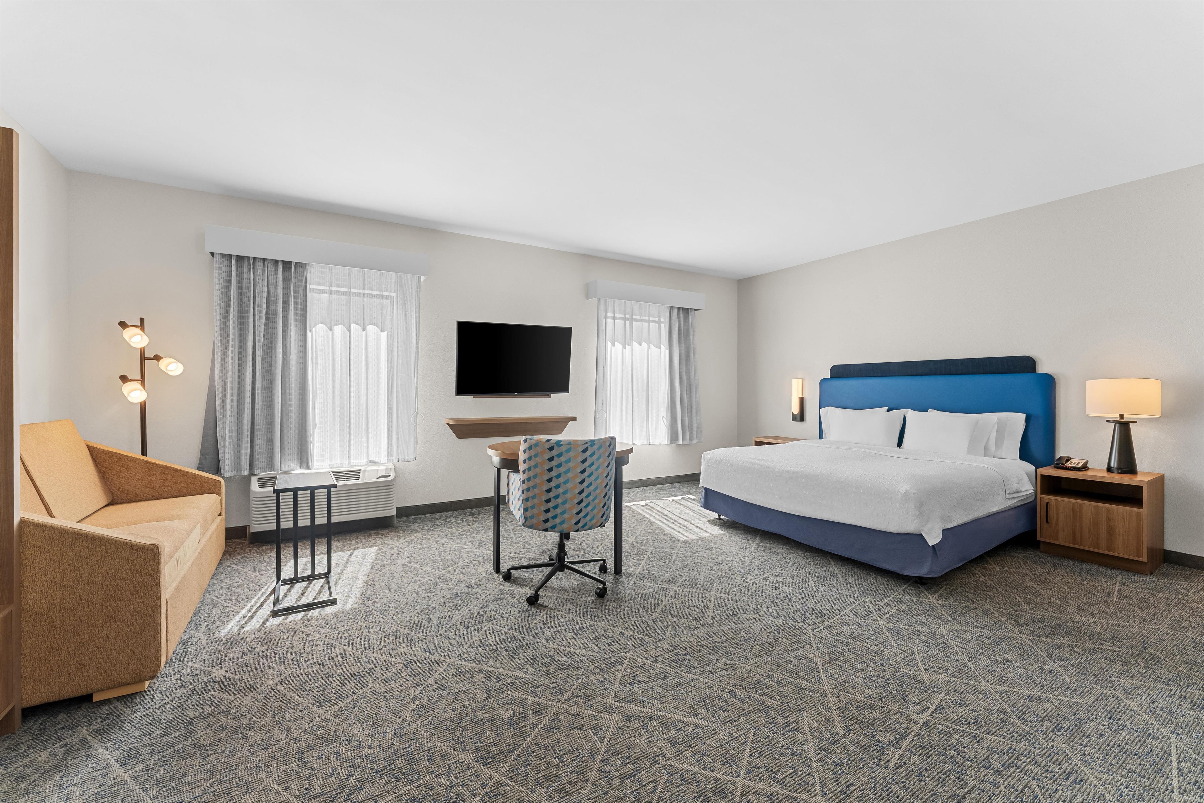 A hotel room with a bed, a desk, a chair, a TV, and a lamp.