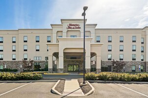 Entrada de un hotel con un letrero que dice 'Hampton Inn Suites' y un estacionamiento al frente.