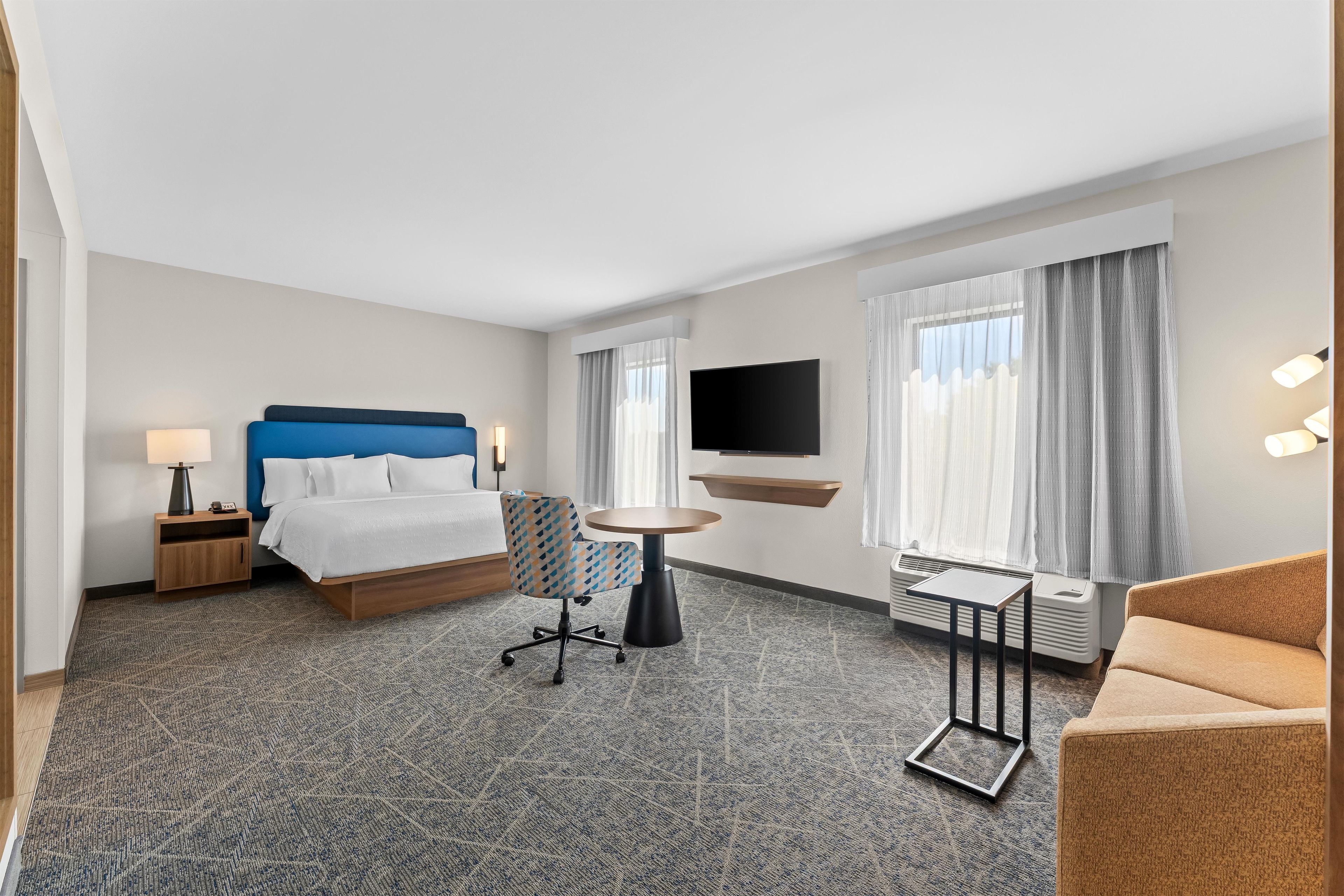 Una habitación de hotel con cama, escritorio, silla, televisor y sofá.