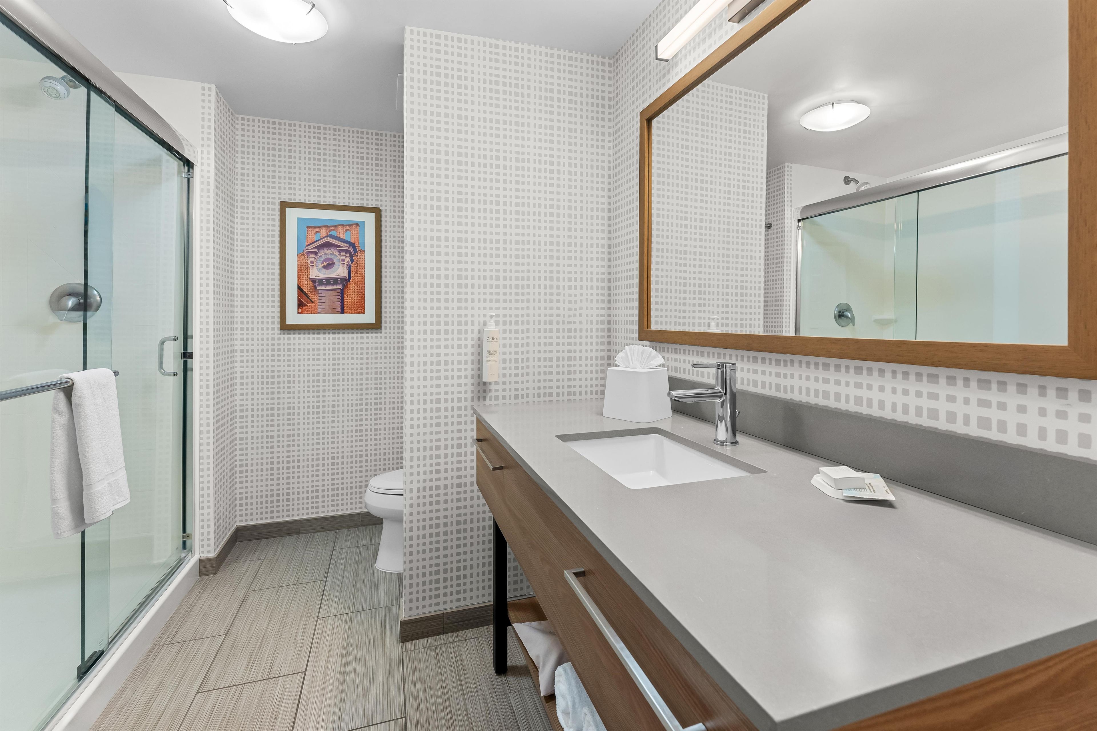 A modern bathroom with a glass shower enclosure, a large mirror, a sink with a wooden vanity, and a toilet.